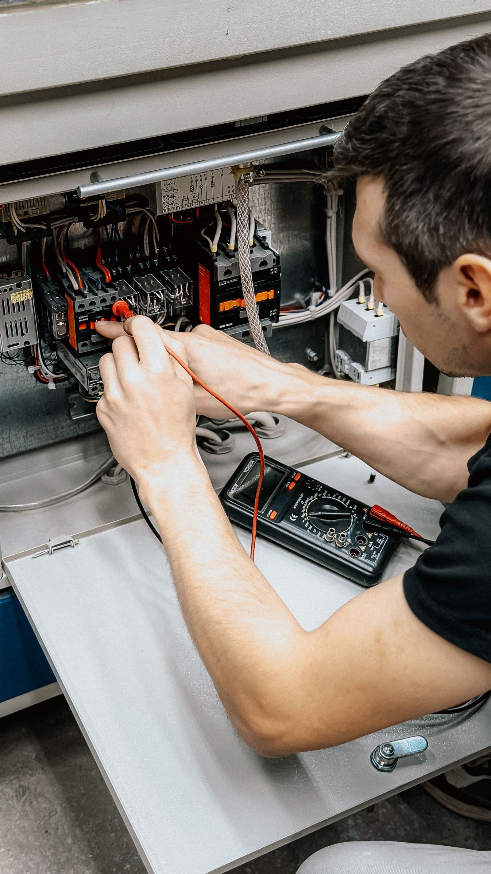 Electrician using a multimeter to test and diagnose an open electrical panel